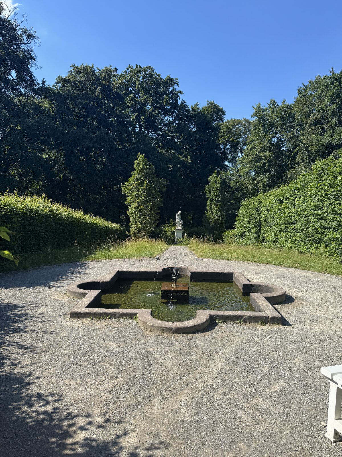 Brunnen im Innenbereich mit springendem Wasser, im Hintergrund eine kleine weiße Statue